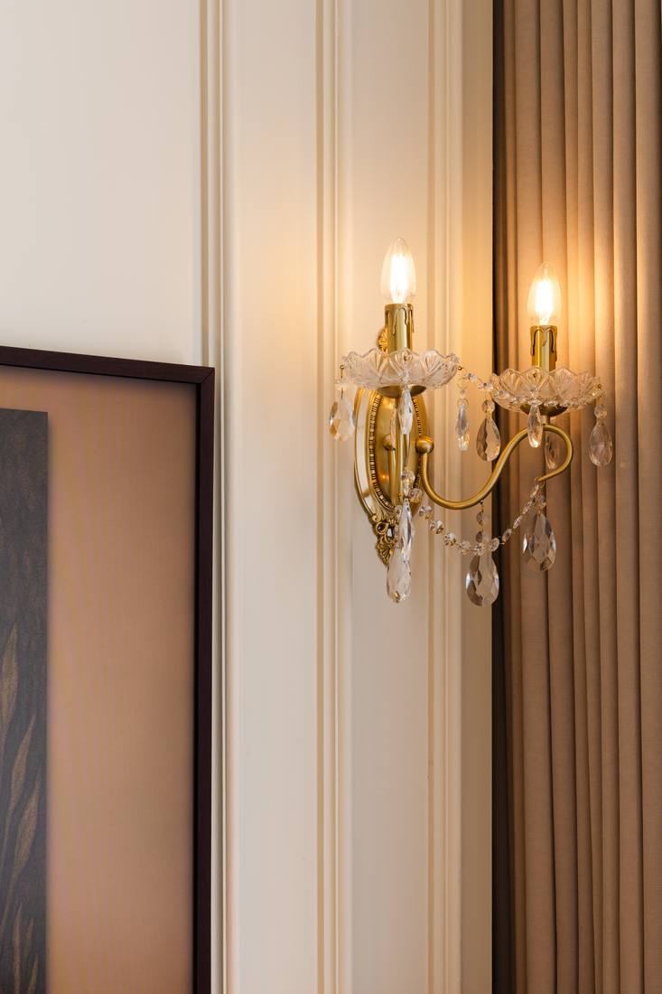 A crystal sconce lit against fluted drapery
